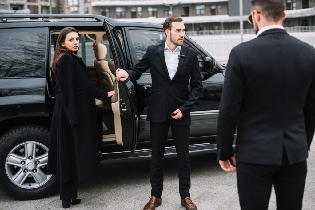 Two professional security guards escorting a woman to a car as part of a chauffeur service.
